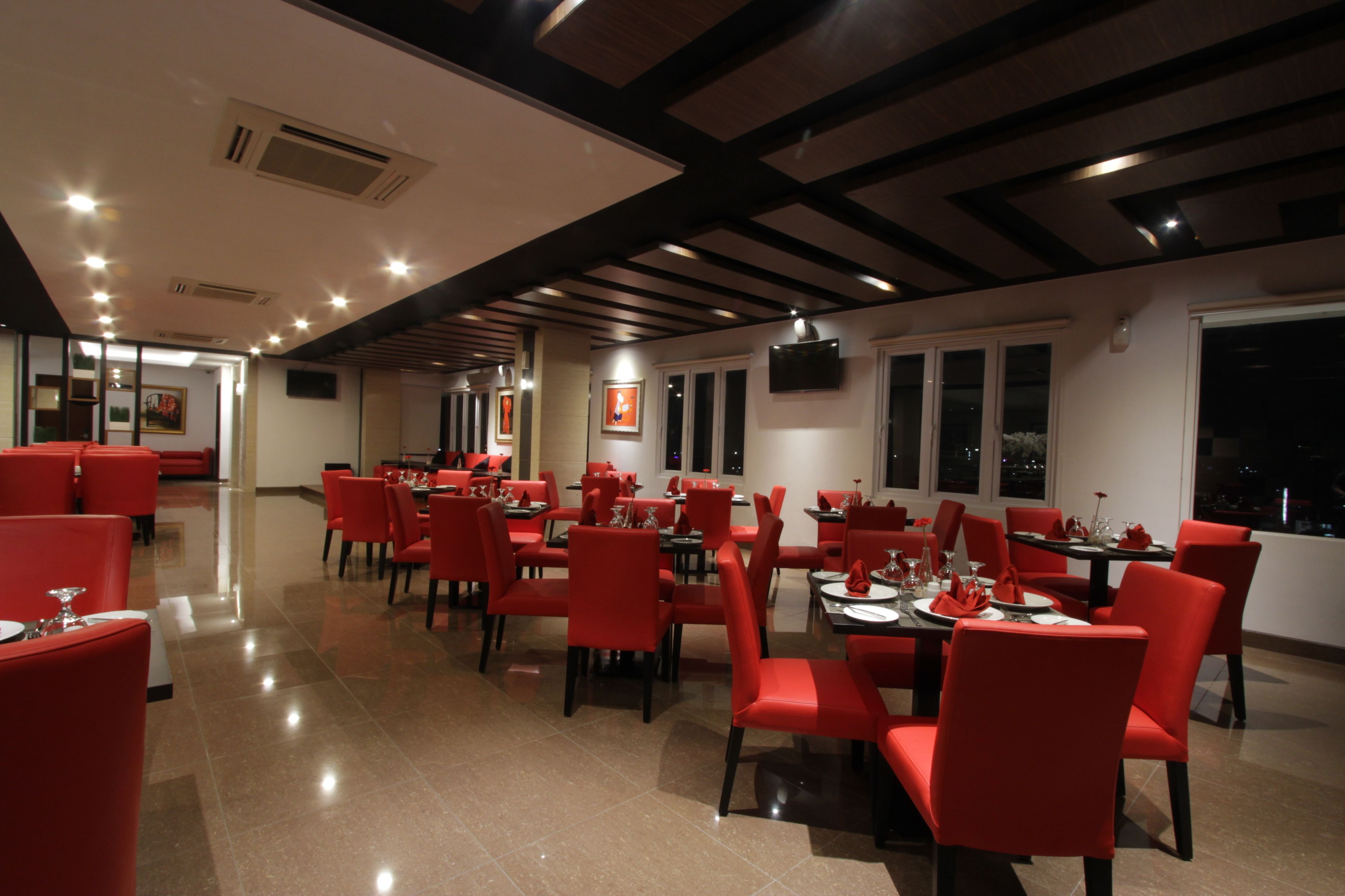 A restaurant with red chairs and tables, a tiled floor, and a modern ceiling design.