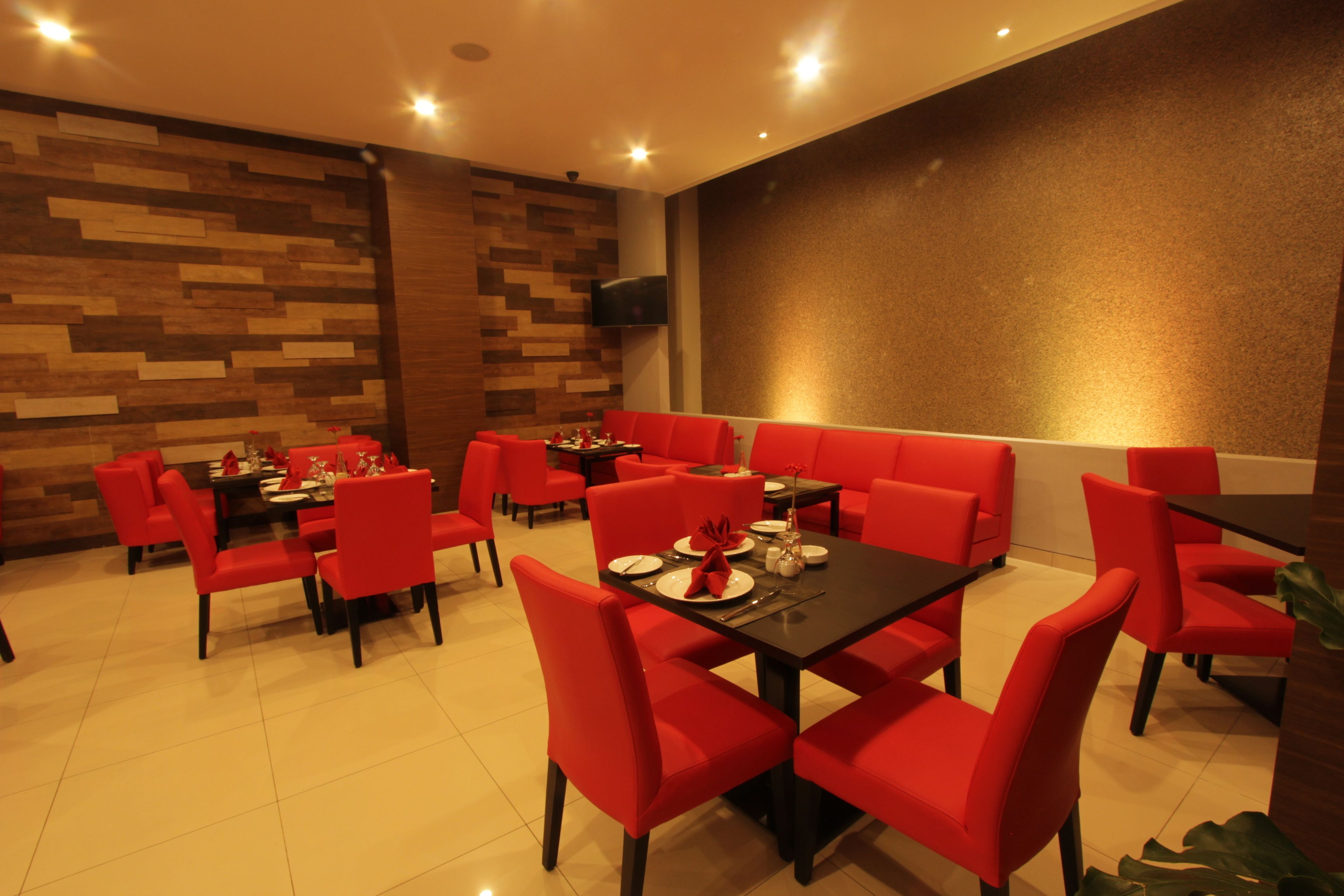 A restaurant with red chairs and black tables, wooden wall decor, and a flat-screen TV on the wall.