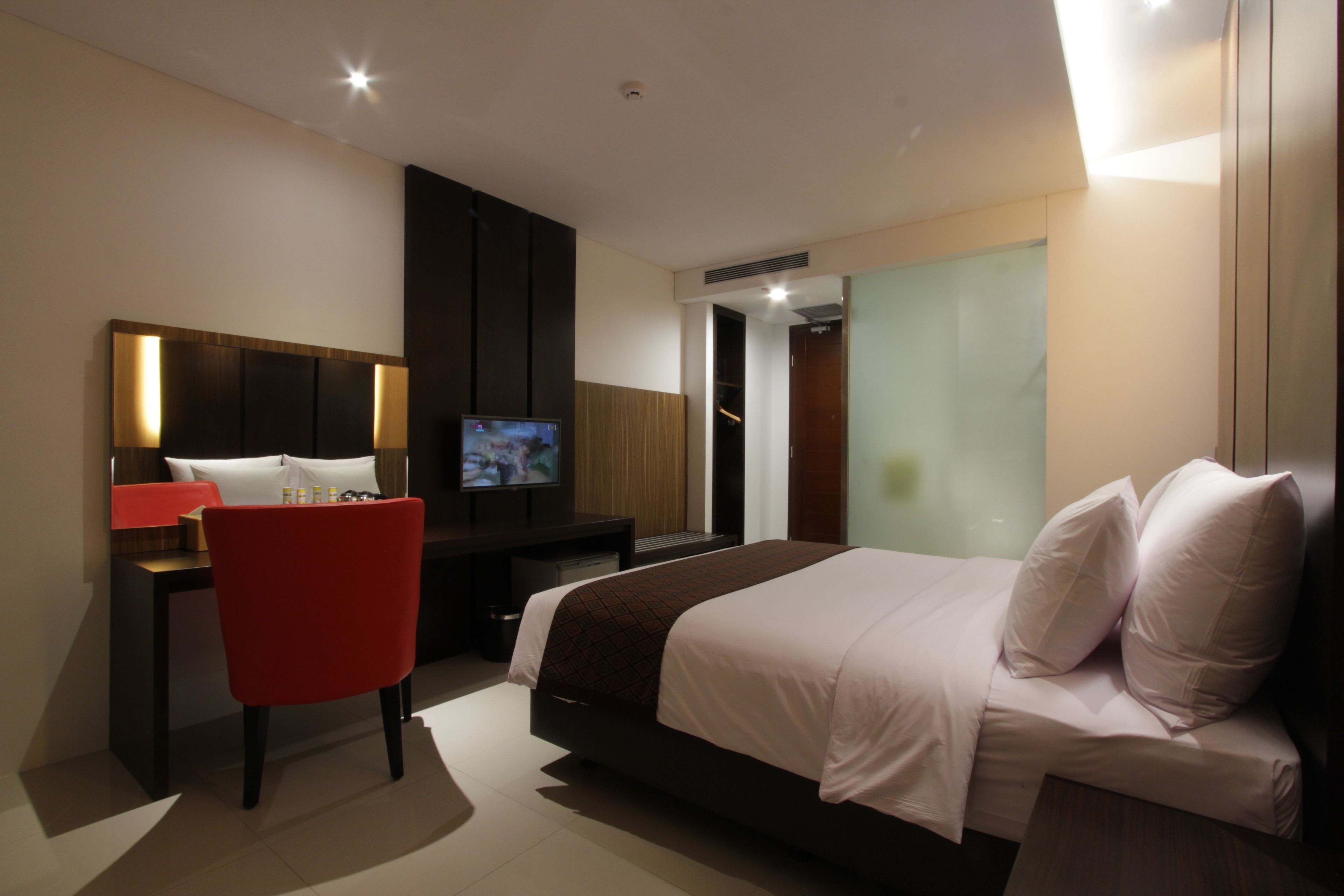 Habitación de hotel moderna con una cama grande, un escritorio con televisor y una silla roja.