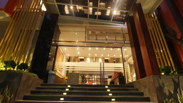 Een hotelentree met een trap naar de lobby, uitgevoerd in modern design met glazen balustrades en een rood tapijt.