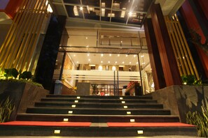 Entrada de un hotel con una escalera que lleva al vestíbulo, con un diseño moderno, barandillas de cristal y una alfombra roja.