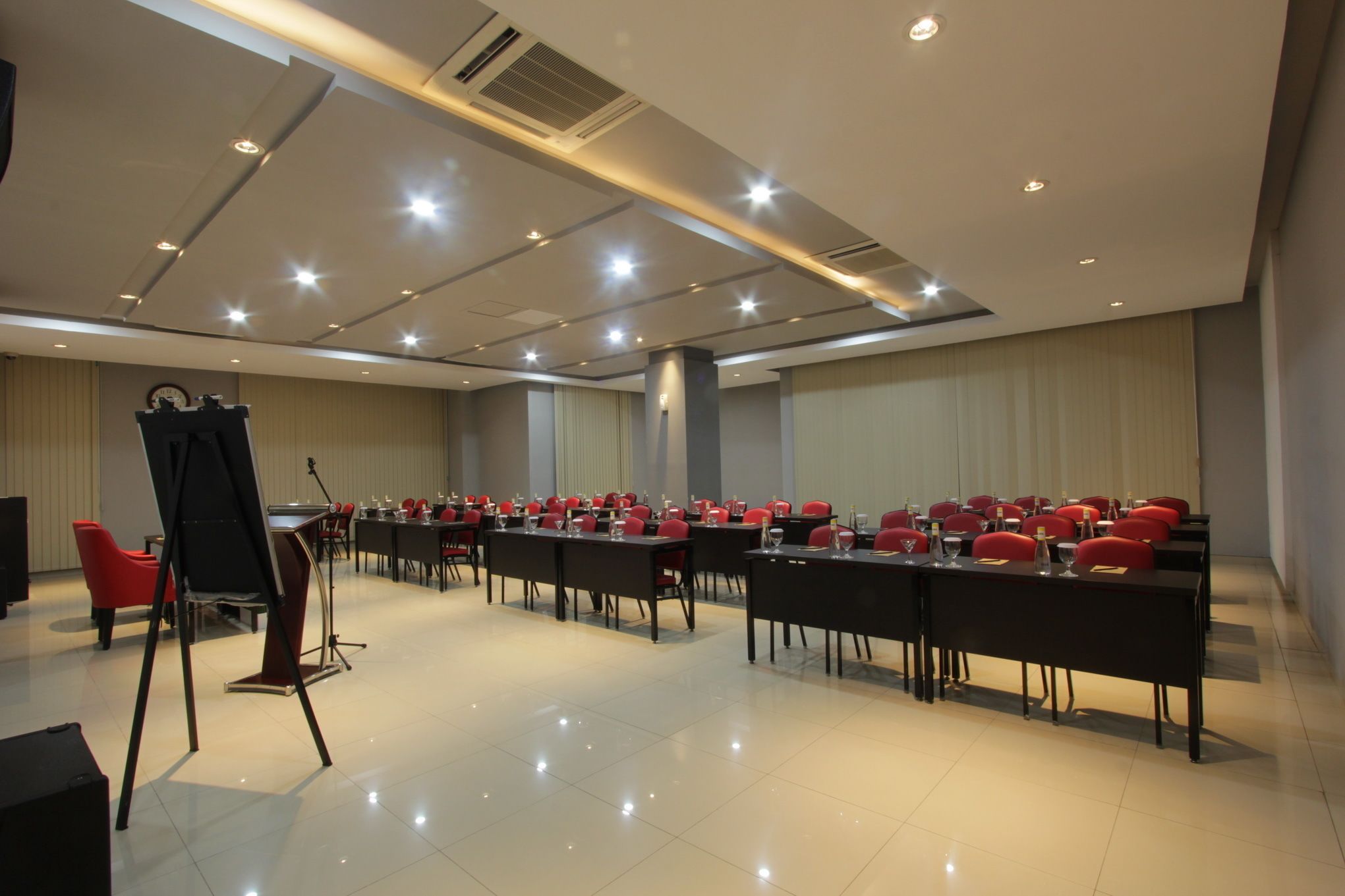 A conference room with multiple tables and red chairs, equipped with microphones and a podium.