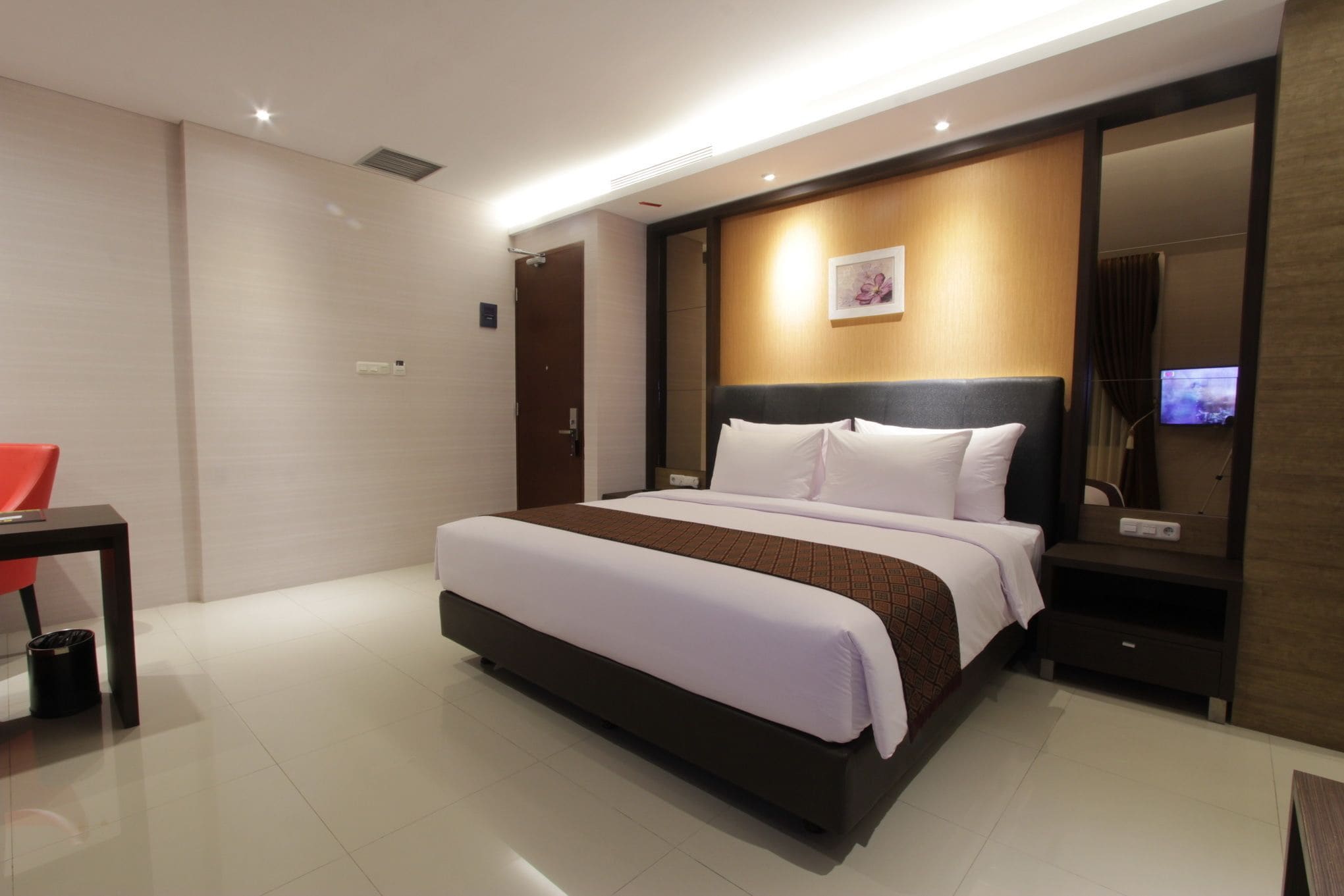 A modern hotel room with a large bed, a bedside table, a TV, and a mirror.