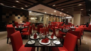 Een restaurant met rode stoelen en zwarte tafels, met een modern interieur en een behangpatroon van ruitjes, en een plafond met houten balken.