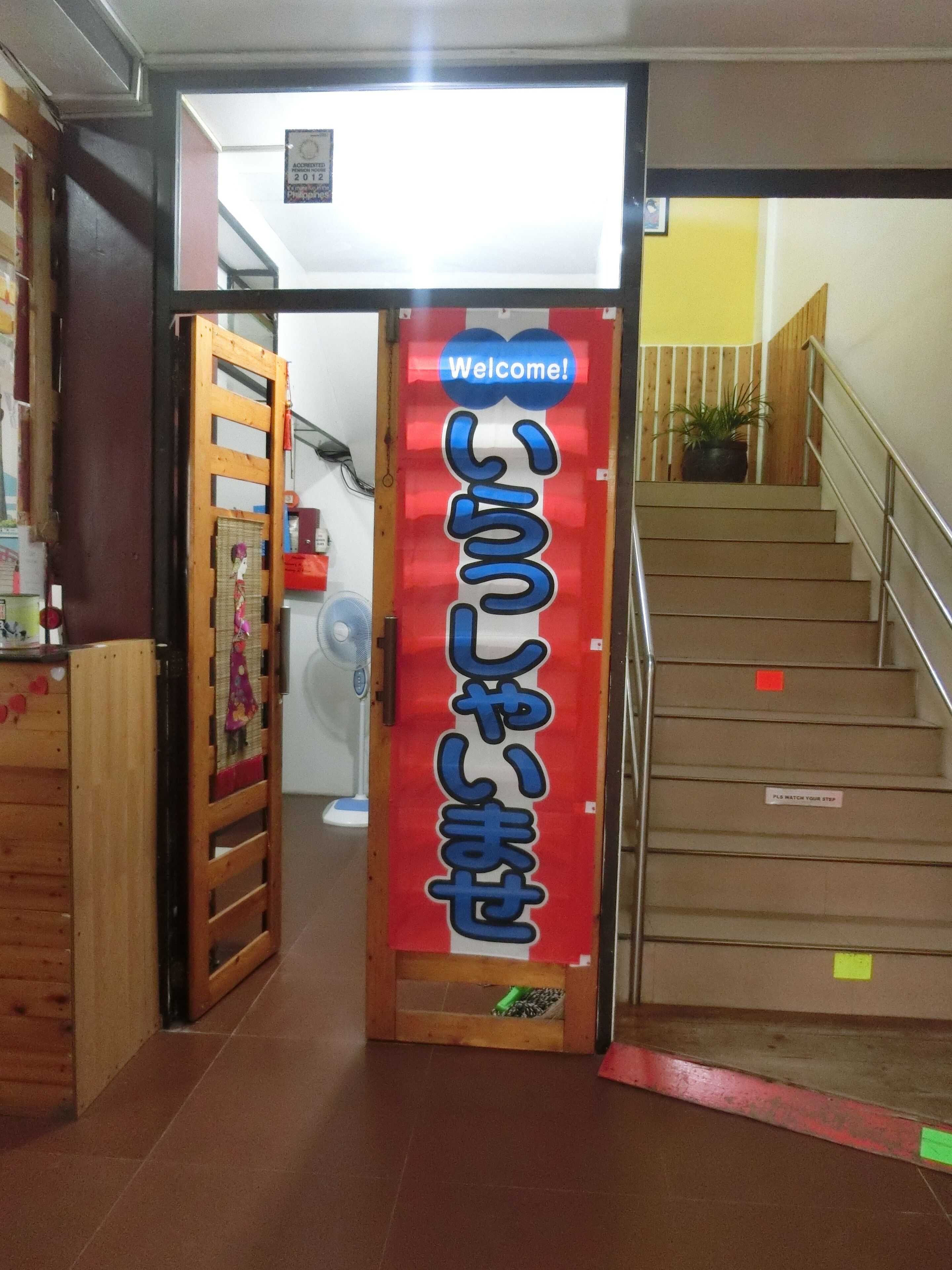 A staircase with a red and white sign reading "Welcome!" and Japanese text.
