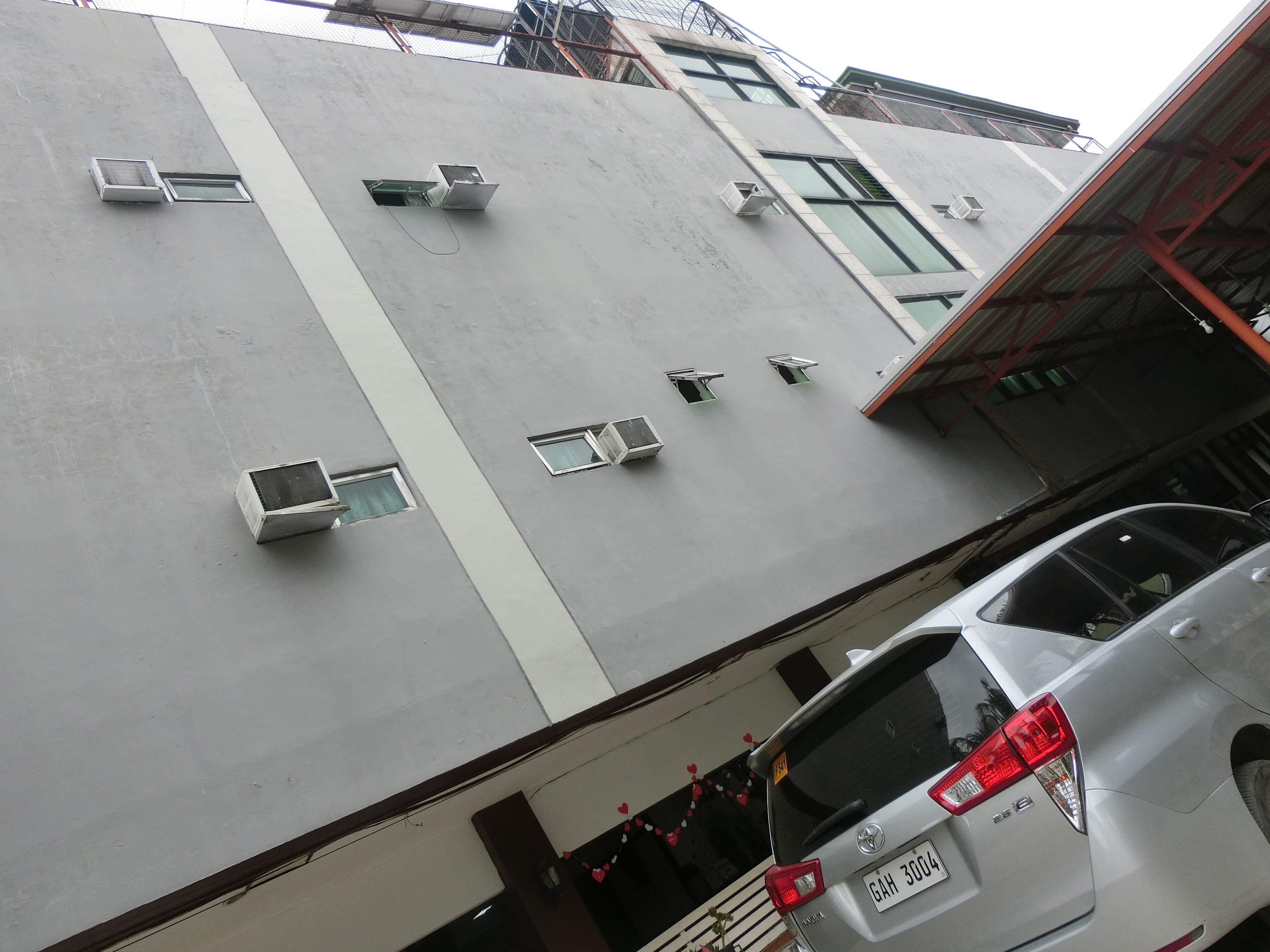 A multi-story building with air conditioning units on the exterior walls, a parking area with a white car, and a visible garage entrance.