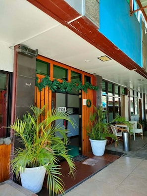Entrada de hotel con fachada de madera, un cartel que dice 'ABRIR' y plantas en macetas.