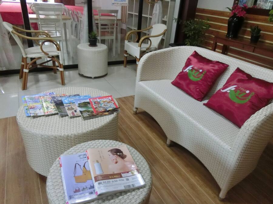 Una stanza con un divano bianco, due poggiapiedi rotondi in vimini e un tavolino con riviste e una brochure.