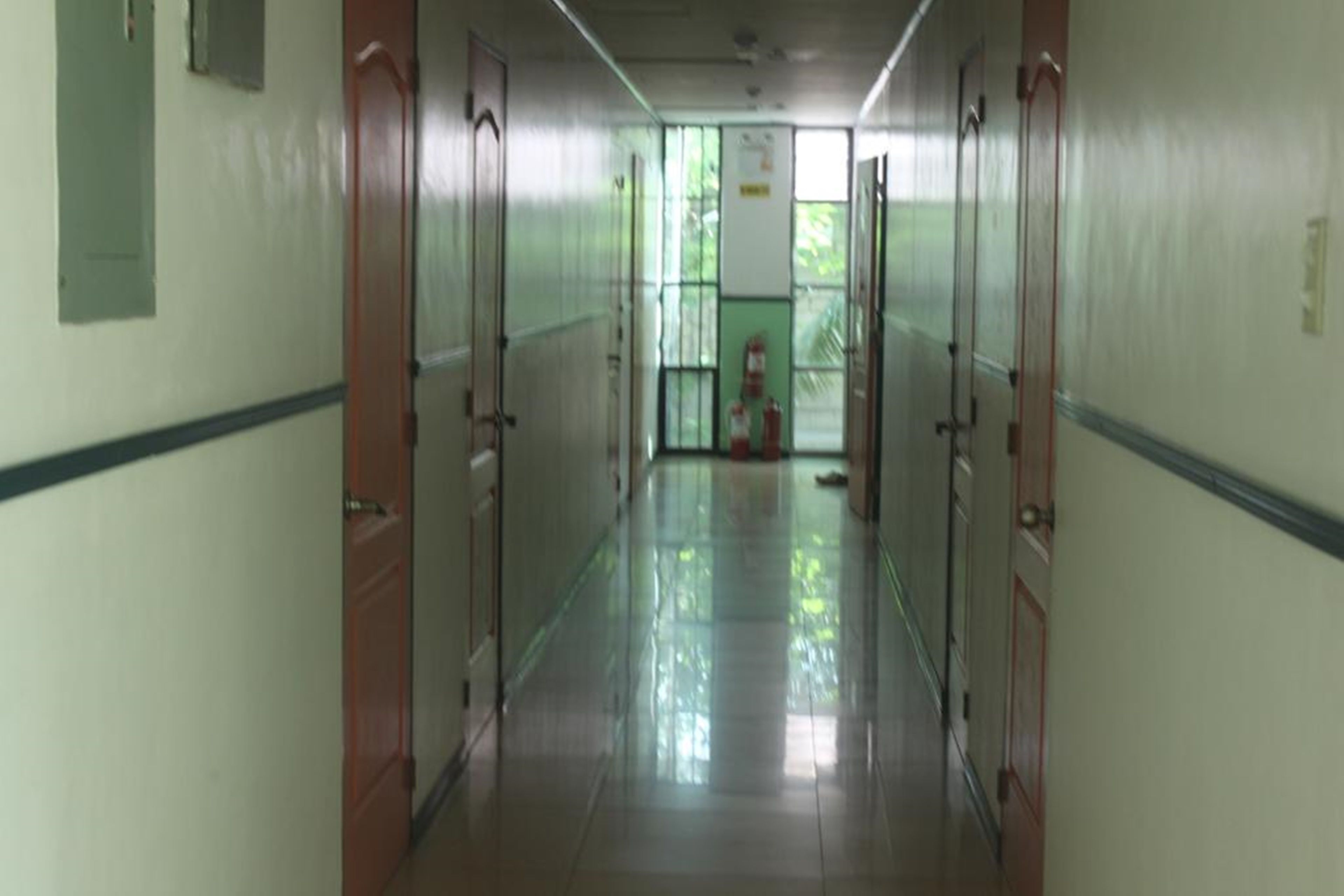 A long, narrow hallway with doors on both sides, a tiled floor, and a fire extinguisher mounted on the wall.