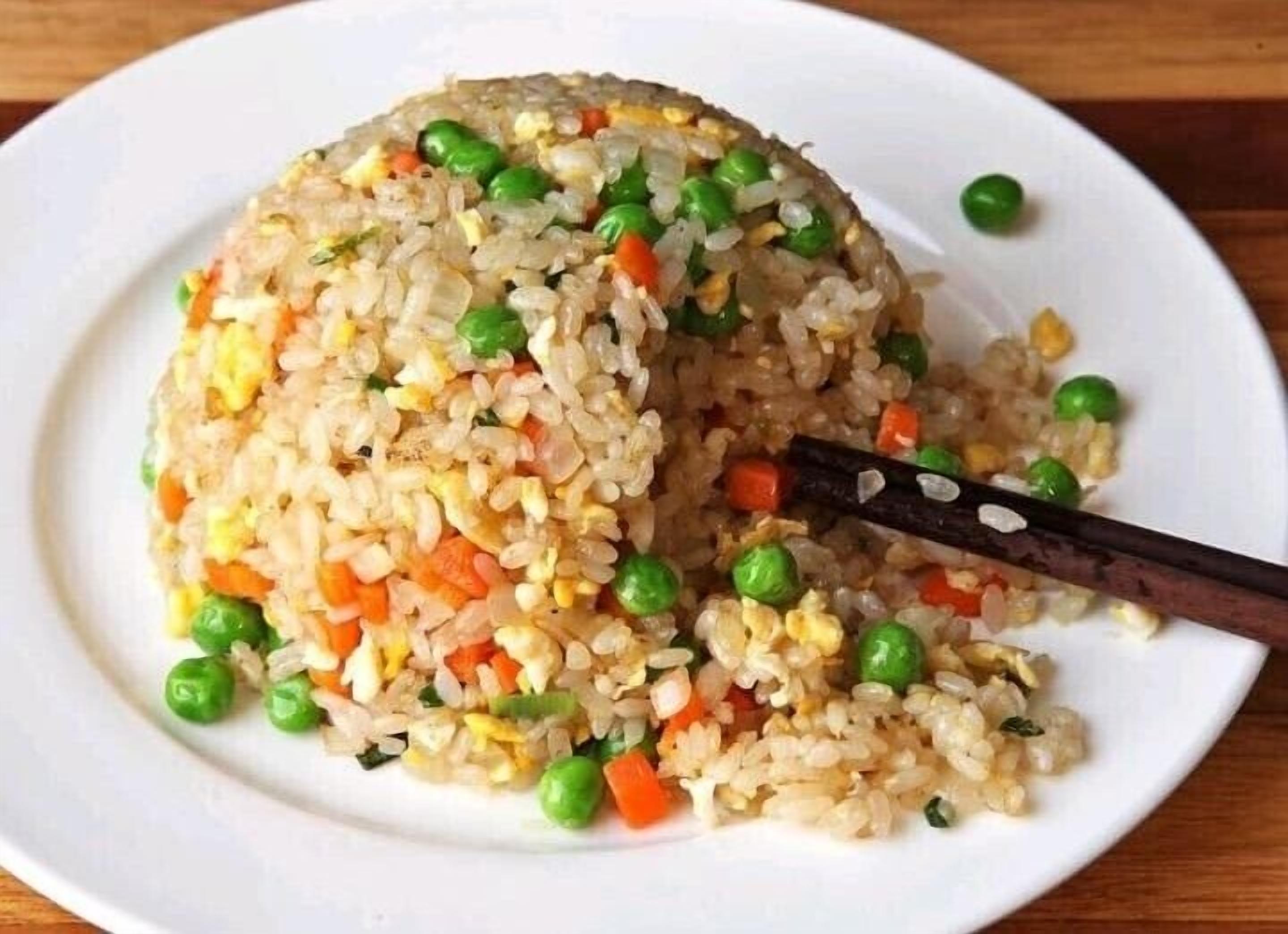 A plate of fried rice with peas and carrots.