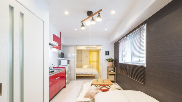 A compact hotel room with a kitchenette, a bed, a bedside table, and a window with blinds. - JESUS SQUARE Nippombashi (Osaka)