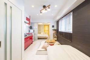 A compact hotel room with a kitchenette, a bed, a bedside table, and a window with blinds. - JESUS SQUARE Nippombashi (Osaka)
