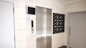 An elevator with a digital display, a control panel, and a decorative panel on the wall. - JESUS SQUARE Nippombashi (Osaka)