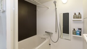A bathroom with a bathtub, a shower, a mirror, and a shelf with toiletries. - JESUS SQUARE Nippombashi (Osaka)