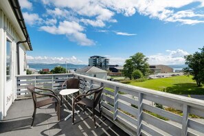 A balcony with wicker chairs and a table, overlooking a grassy area and buildings. - Brekstad Gjestehus (Orland)