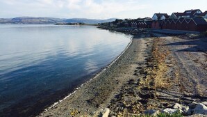 A coastal area with a pebble beach, a row of houses, and a calm sea. - Brekstad Gjestehus (Orland)
