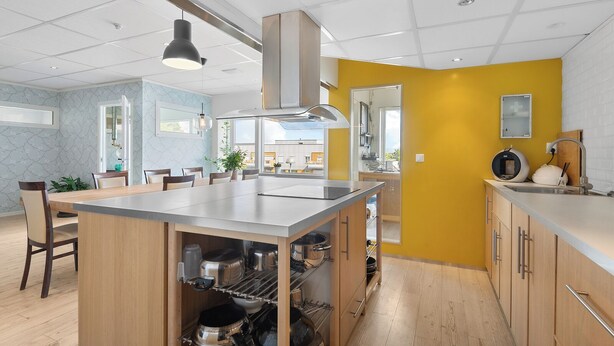 A modern kitchen with a central island, wooden cabinets, and a yellow accent wall. - Brekstad Gjestehus (Orland)