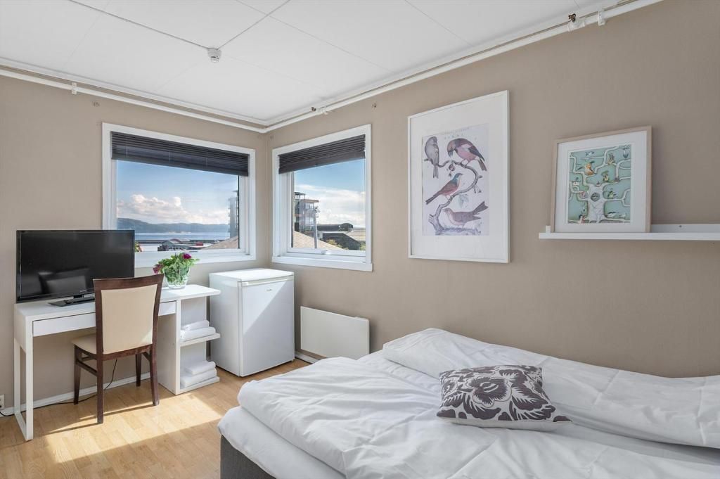 A bedroom with a bed, a desk with a computer, a chair, and artwork on the walls.