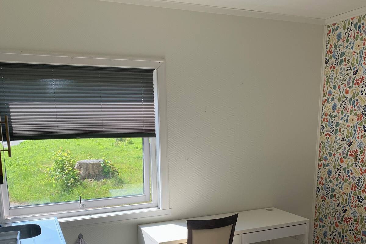 Ein kleines Schlafzimmer mit einem Einzelbett, einem Schreibtisch und einem Stuhl. Ein Fenster mit Jalousien bietet Blick ins Freie.