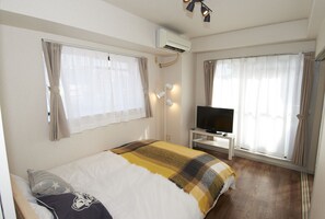 Une chambre d’hôtel avec un lit, un téléviseur posé sur un meuble et un climatiseur fixé au mur.