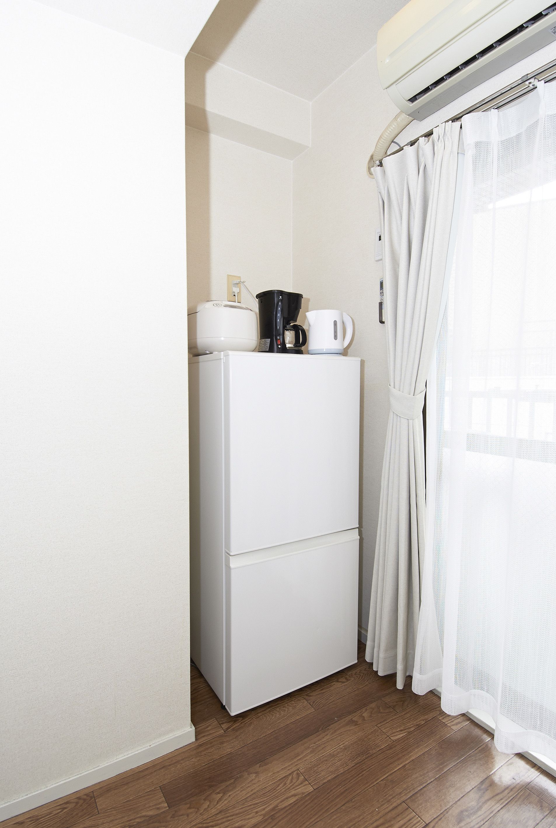A compact kitchenette with a white refrigerator, a coffee maker, and a kettle on top.