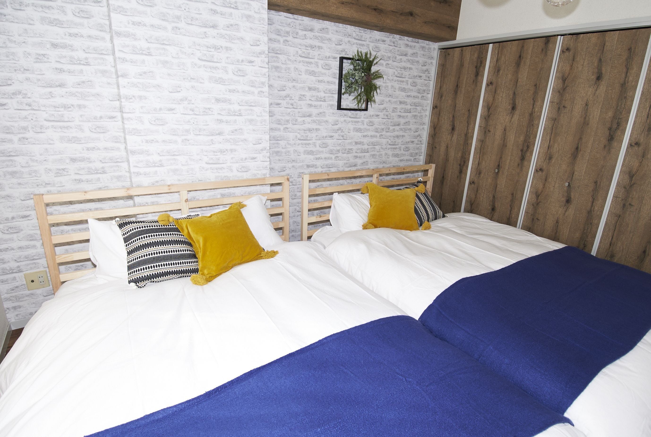 A double bed with white and blue bedding, two wooden headboards, and a brick-patterned wall.