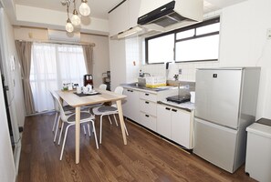 Une cuisine de taille réduite comprenant une table à manger, des chaises, un réfrigérateur et une fenêtre avec des rideaux.