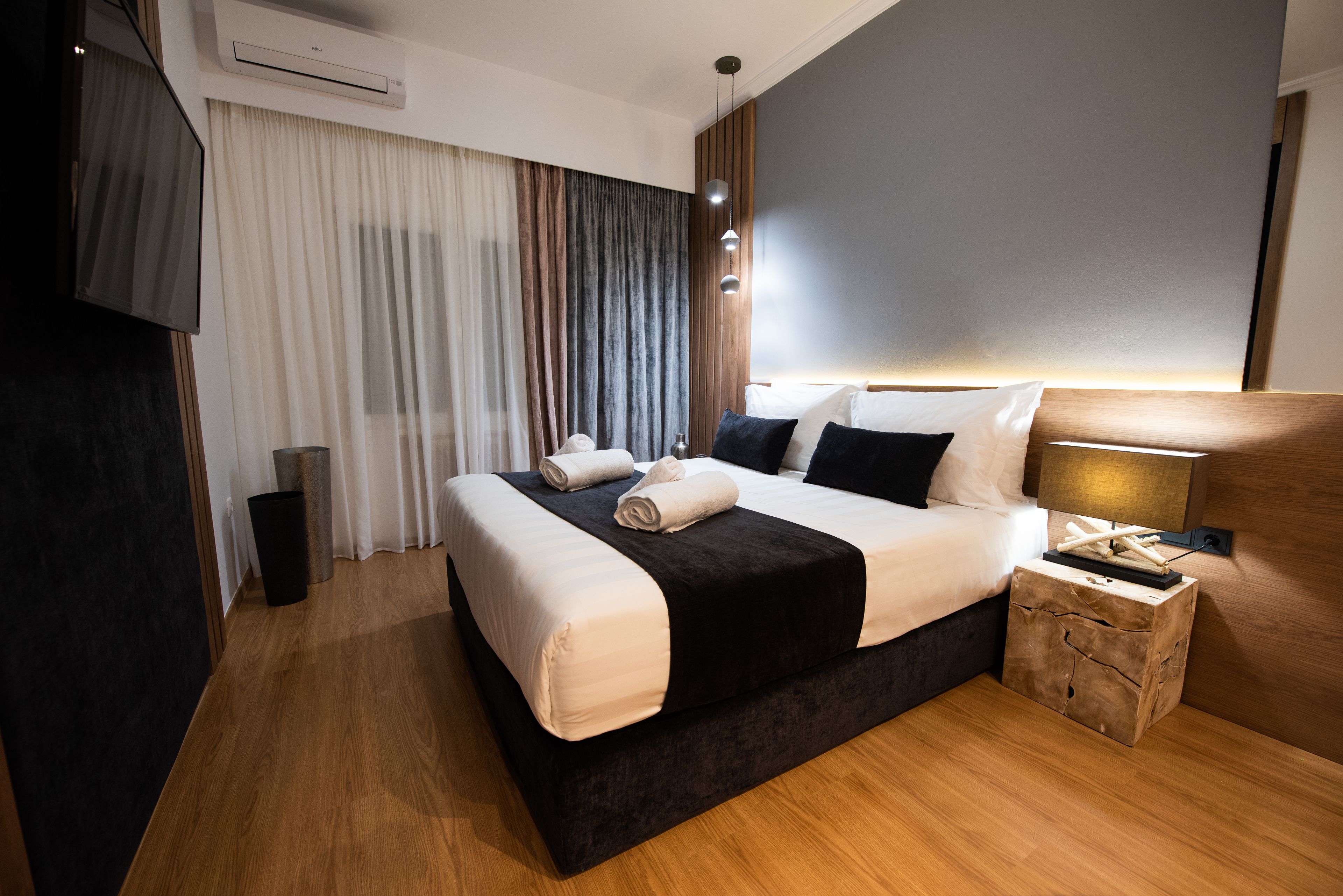 Ein modernes Hotelzimmer mit einem großen Bett, einem Nachttisch, einer Lampe und einem an der Wand montierten Fernseher.