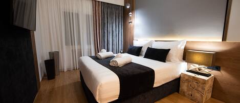 A modern hotel room with a large bed, a bedside table, a lamp, and a TV mounted on the wall.