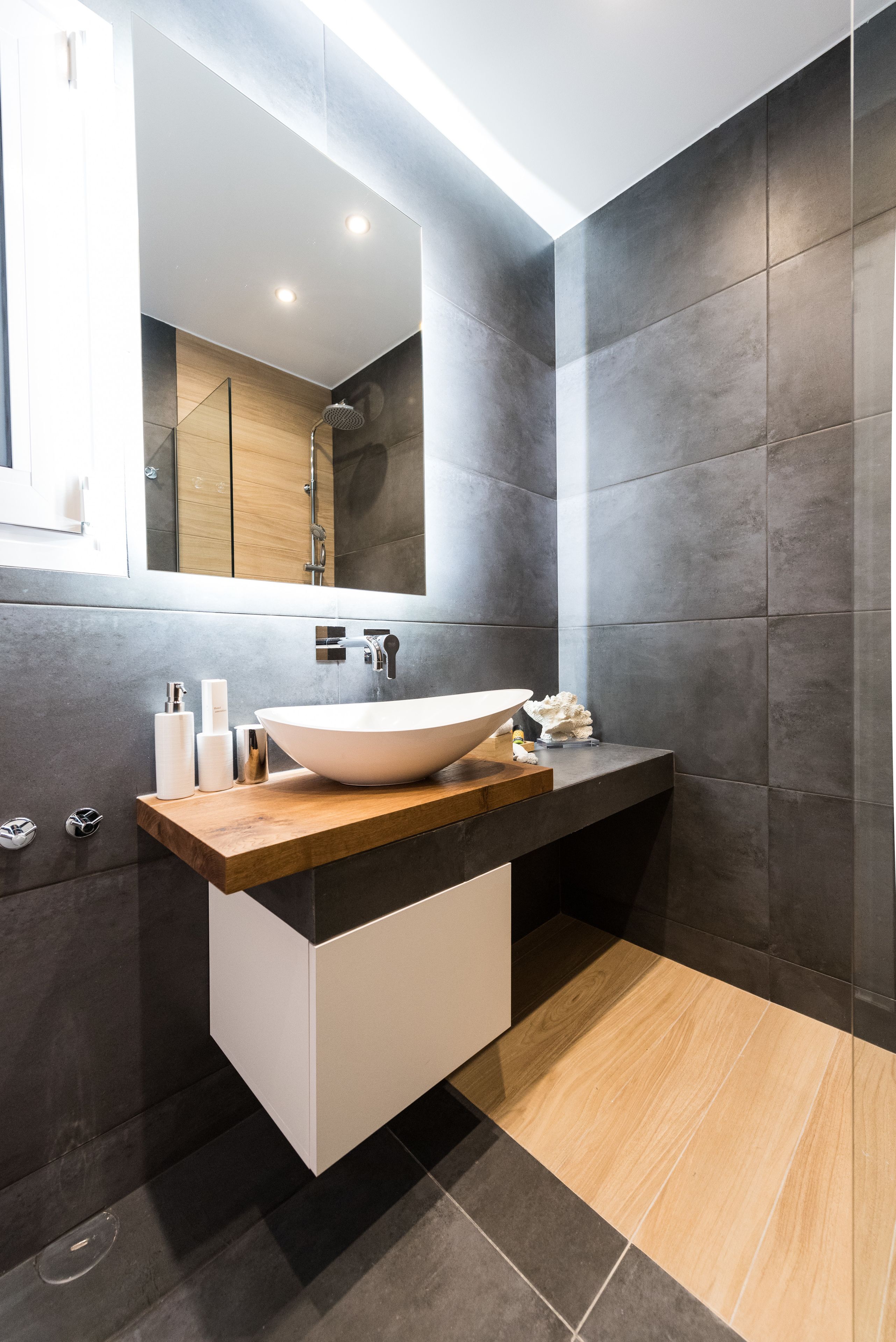 Une salle de bain moderne avec un grand lavabo blanc, des murs recouverts de carreaux foncés et un plan de travail en bois.