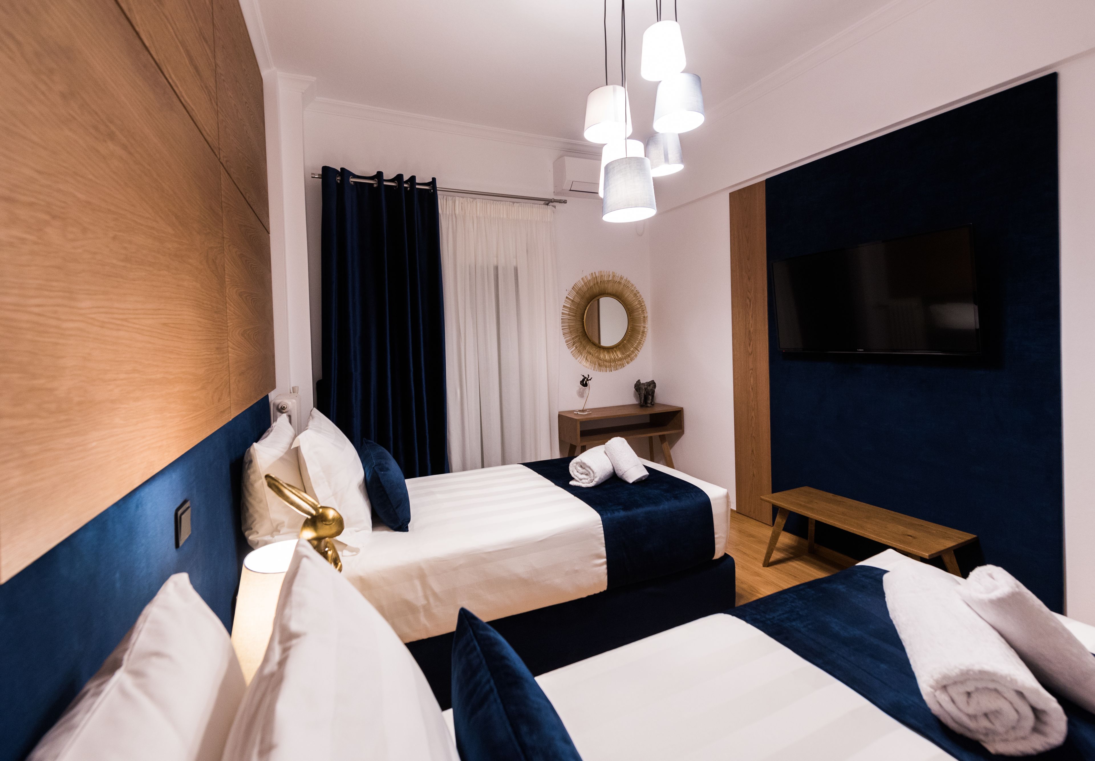 Habitación de hotel con dos camas, cabecera de madera, una mesita con espejo y televisor en la pared.
