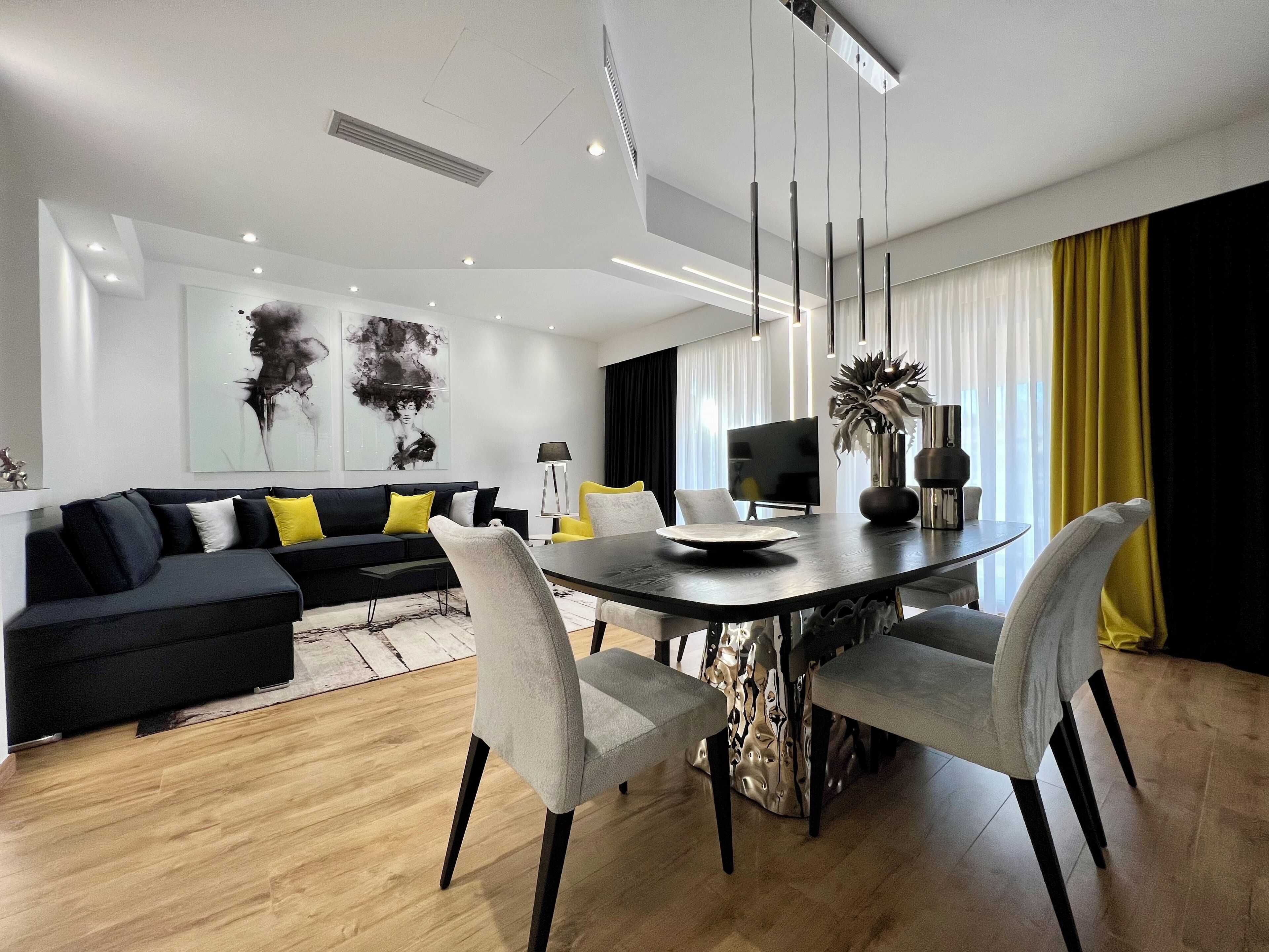 A modern living room with a black sofa, a dining table, and a TV.