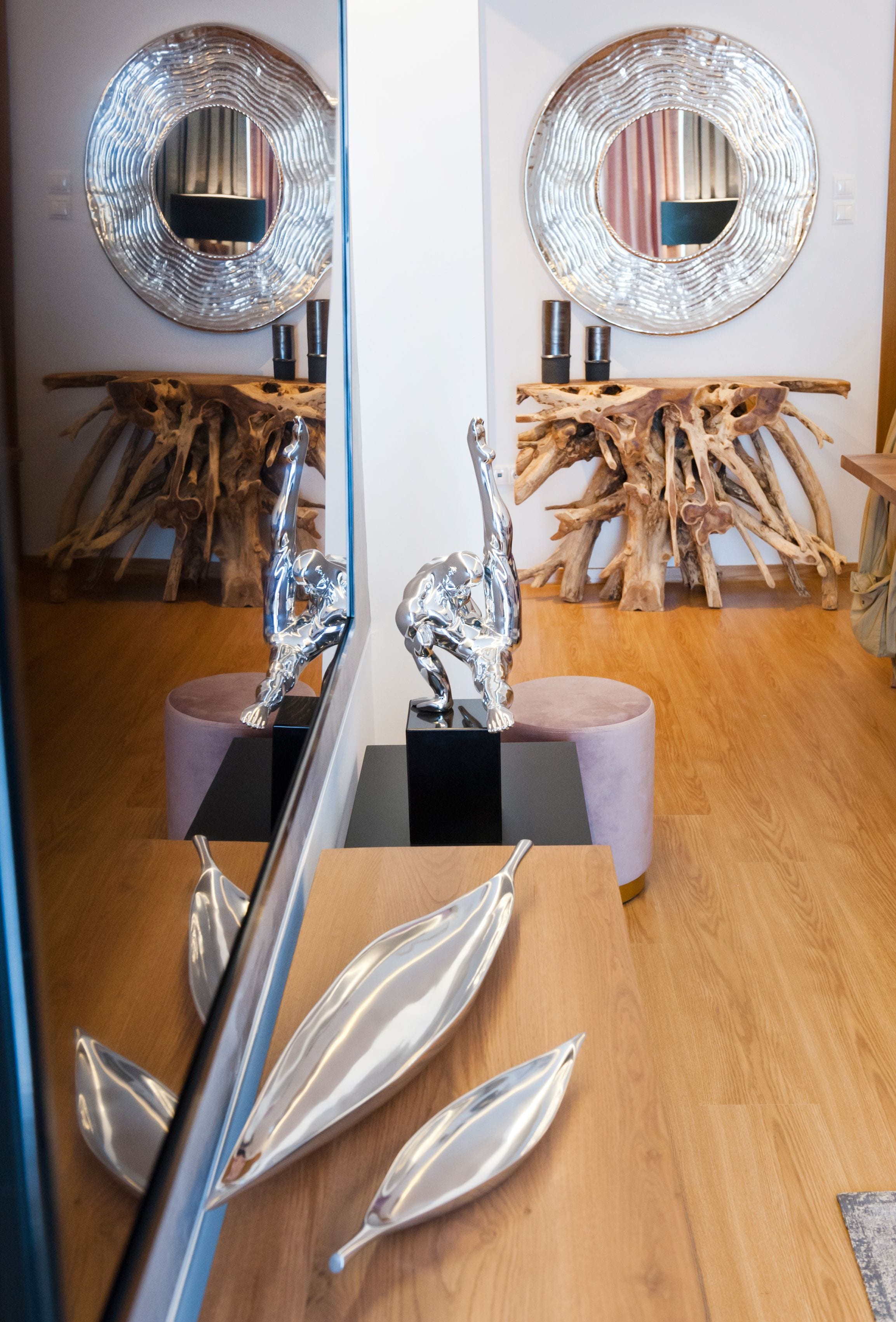 Un intérieur moderne avec un plancher en bois, une sculpture centrale et un grand miroir rond accroché au mur.