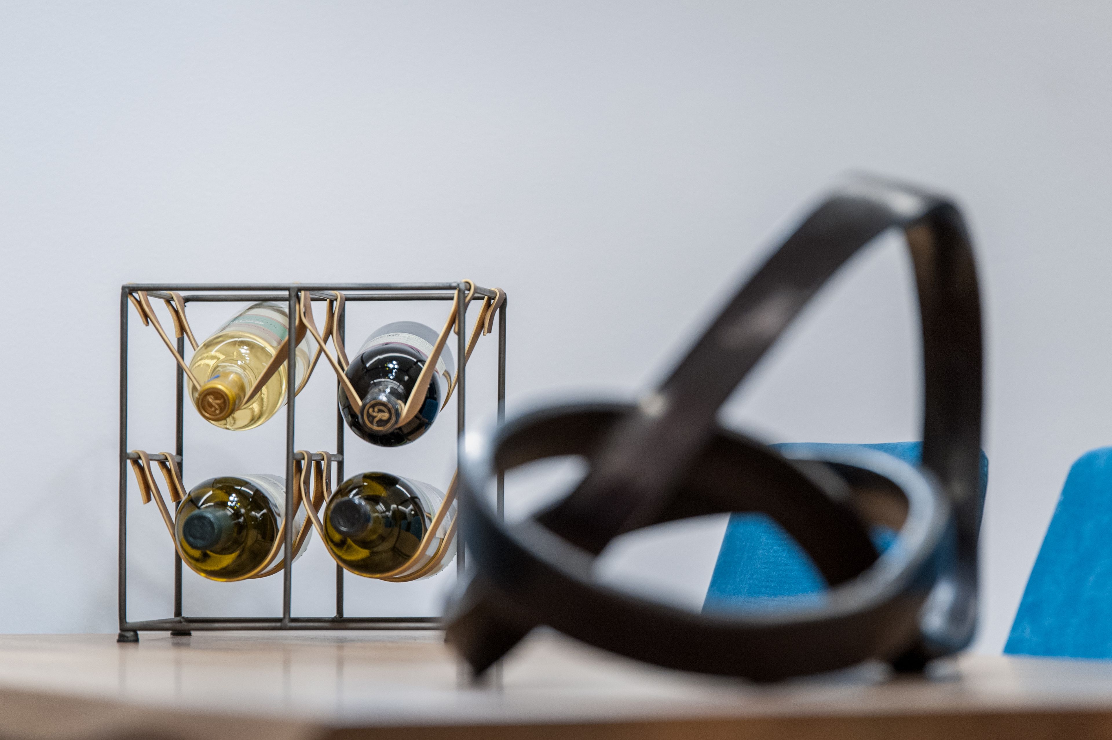 A wine rack with four bottles and a pair of glasses on a table.