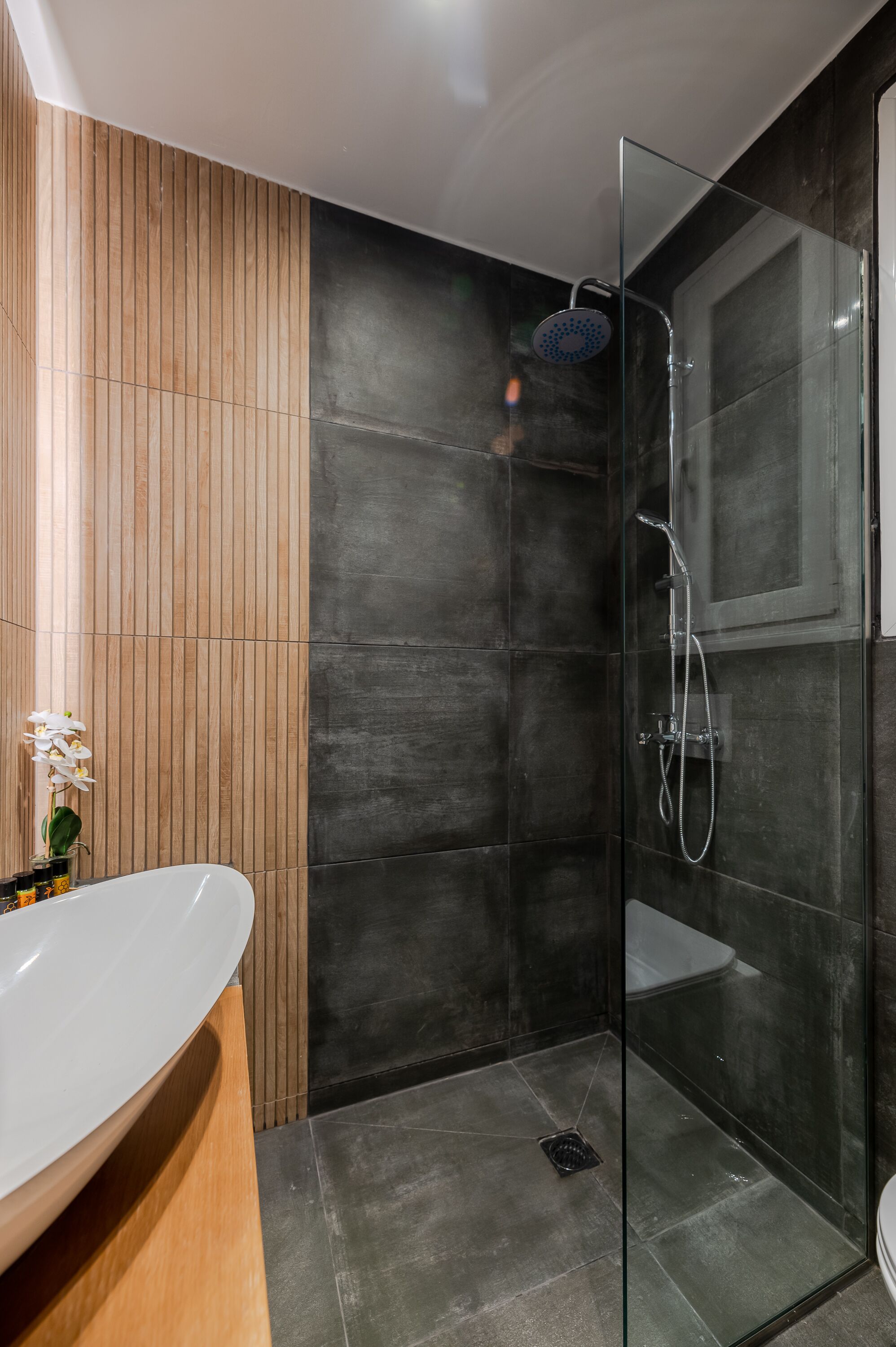 A modern bathroom with a glass-enclosed shower, a wooden vanity, and a white sink.
