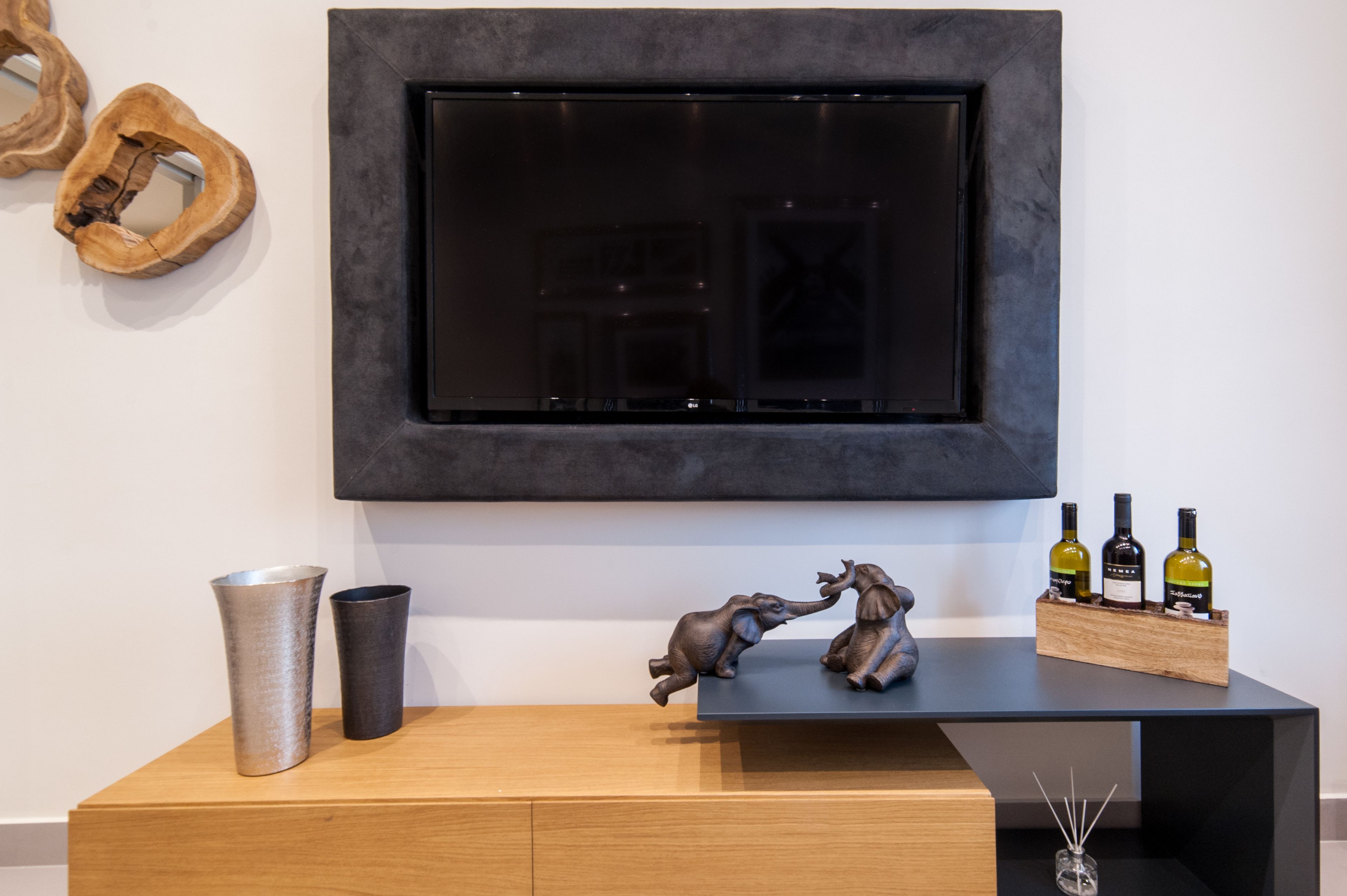 A modern living room with a flat-screen TV mounted on the wall, a wooden console table with decorative items, and a wine rack with bottles.