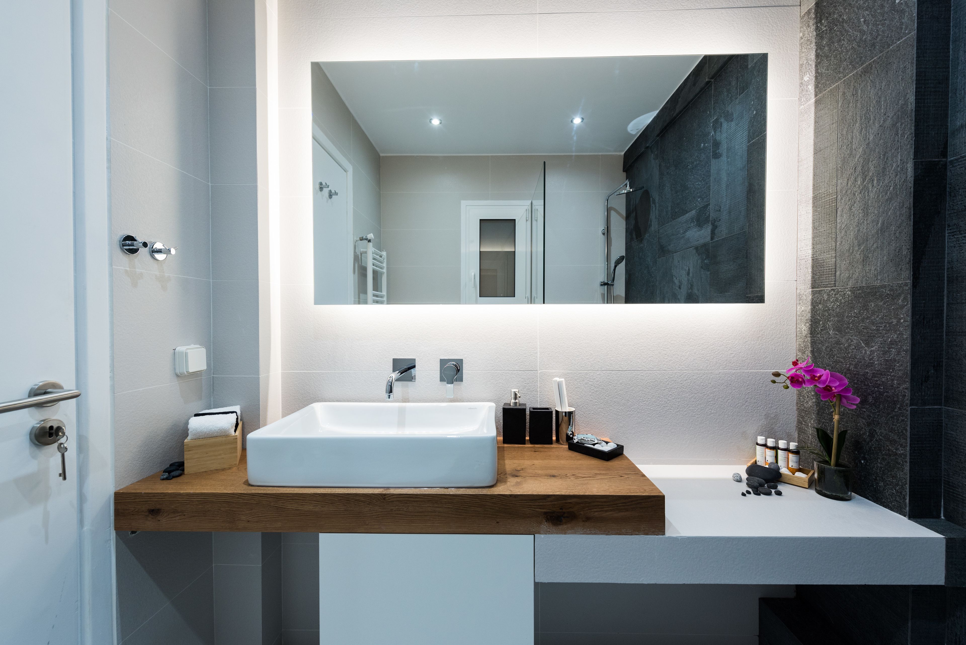 A modern bathroom with a wooden vanity, a white sink, and a large mirror.