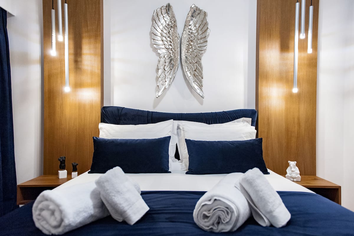 Un lit bien fait, avec une literie blanche et bleue, une paire d’ailes d’ange accrochée au mur et des tables de chevet ornées de petites figurines d’ours.