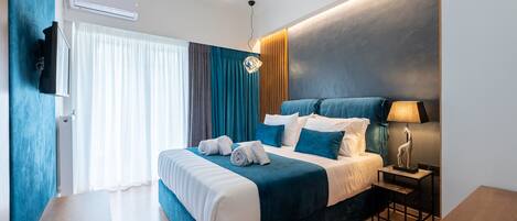 A modern hotel room with a large bed, a flat-screen TV, a desk, and a lamp.