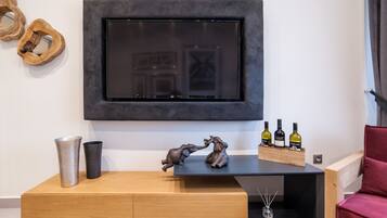 Een moderne woonkamer met een wandtelevisie, een houten console, decoratieve objecten en een rode fauteuil.