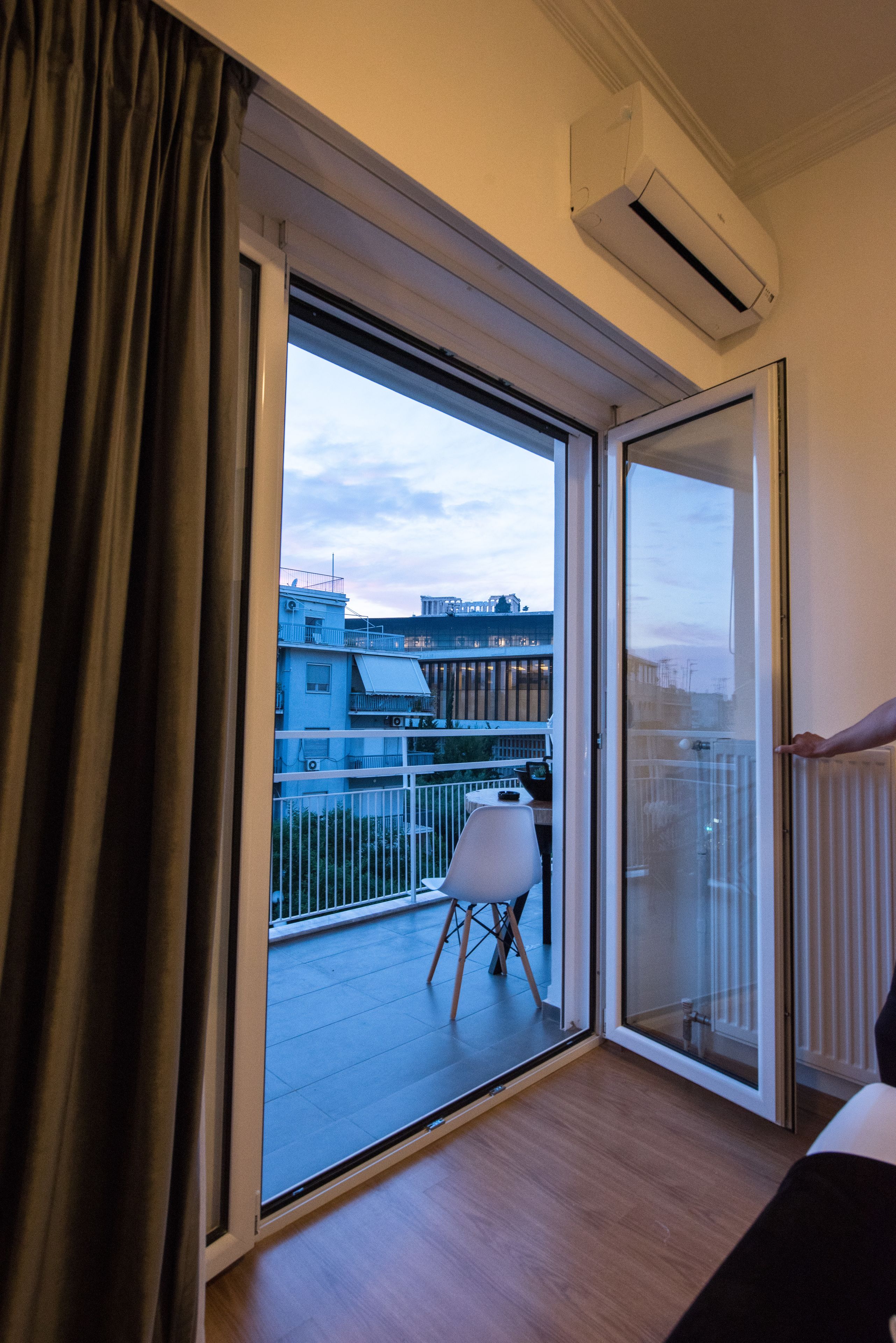 A room with a large sliding glass door leading to a balcony with a white chair and a railing.