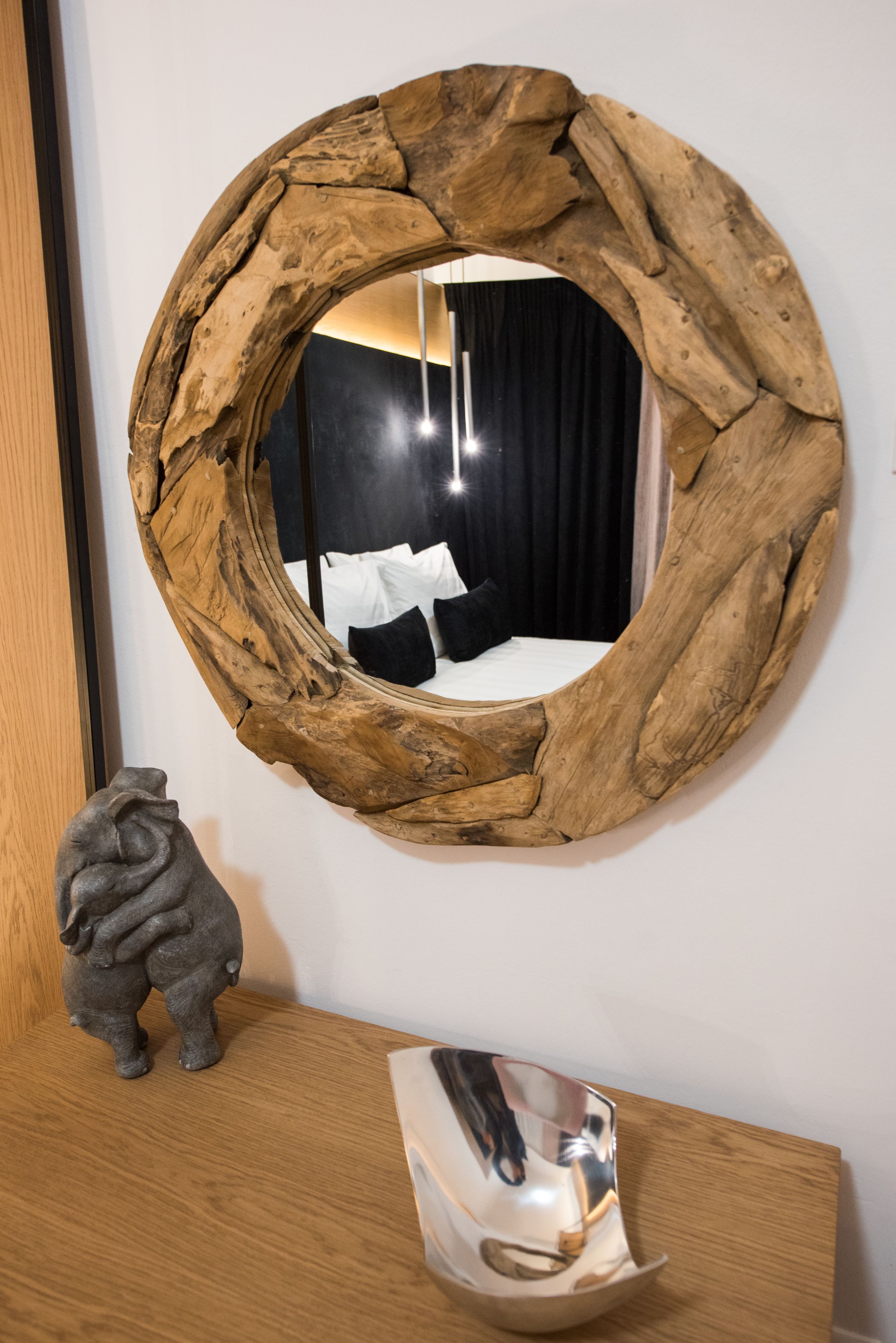 A round mirror with a natural wood frame, a small sculpture, and a reflective object on a wooden surface.