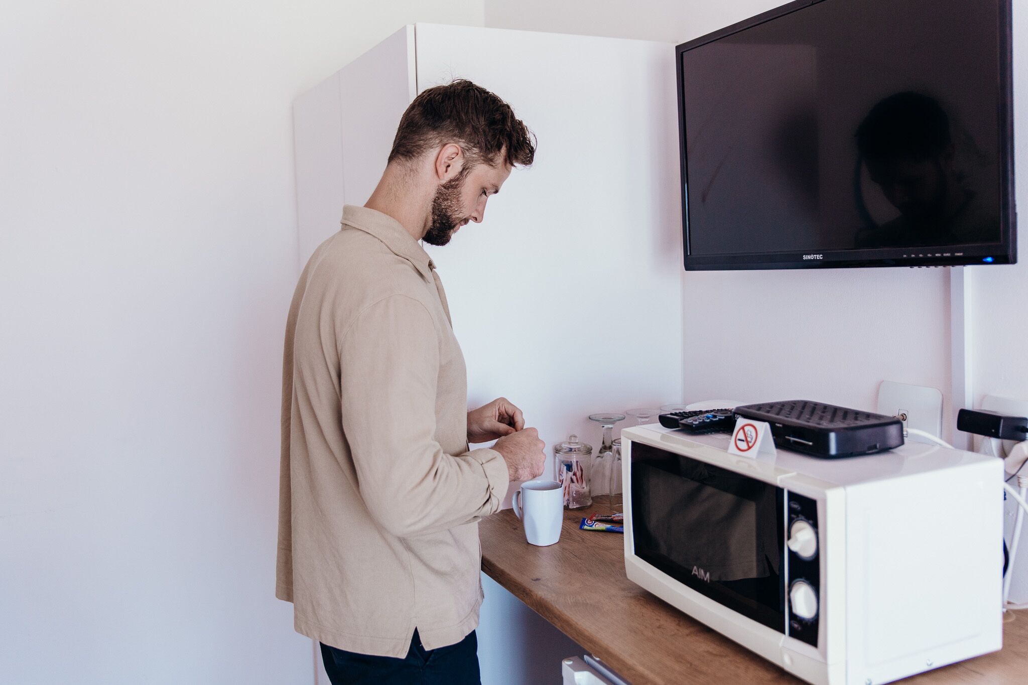 Una persona de pie junto a una encimera de cocina con un microondas, una cafetera y una taza blanca.
