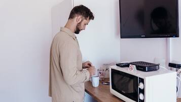 Una persona de pie junto a una encimera de cocina con un microondas, una cafetera y una taza blanca.