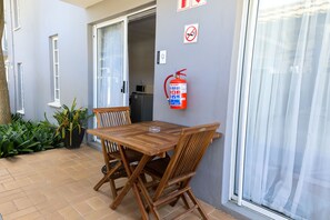 A patio with a wooden table and chairs, a fire extinguisher on the wall, and a sliding glass door. - George Lodge International (George)