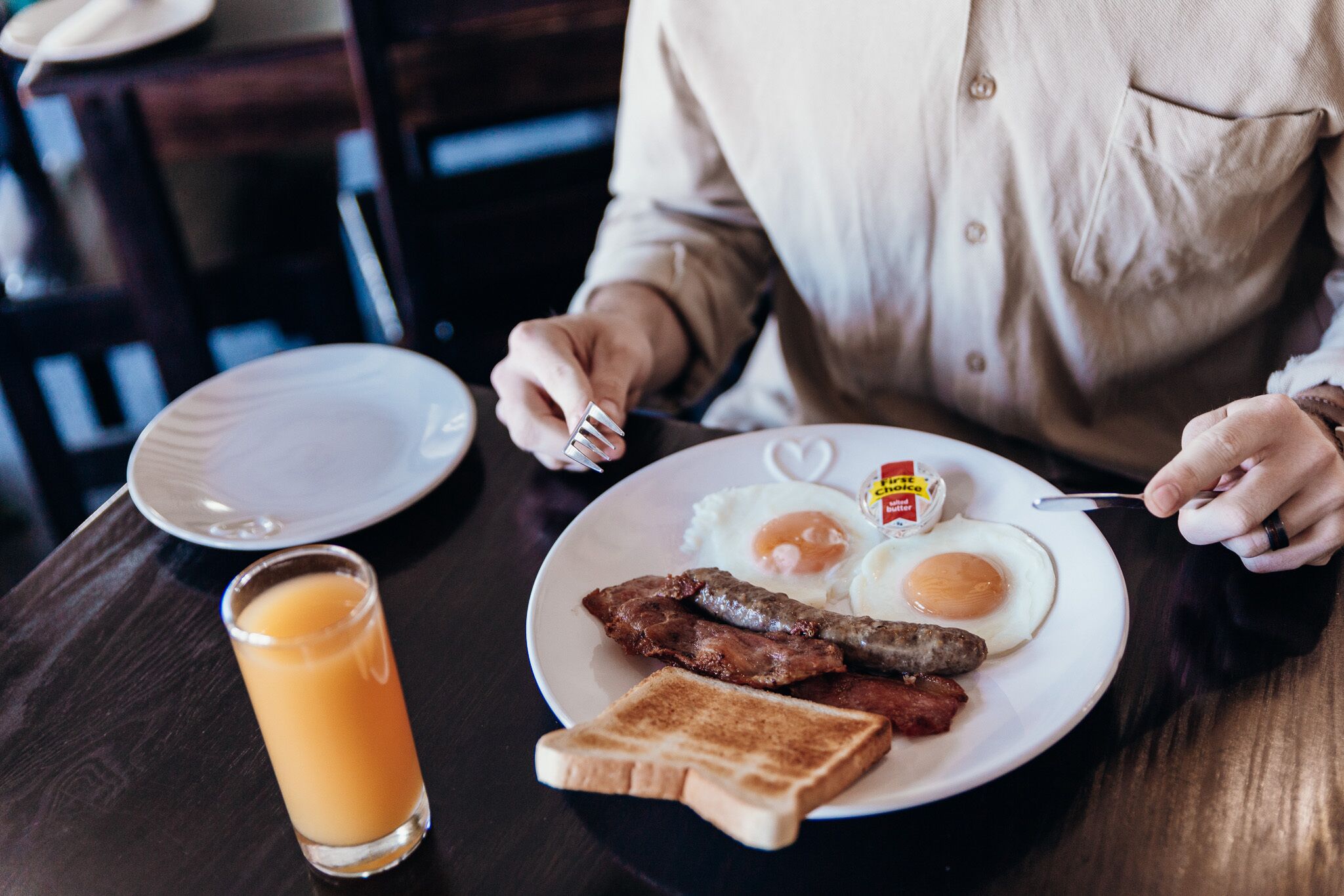 A breakfast plate with eggs, bacon, sausage, toast, and a glass of orange juice on a wooden table.