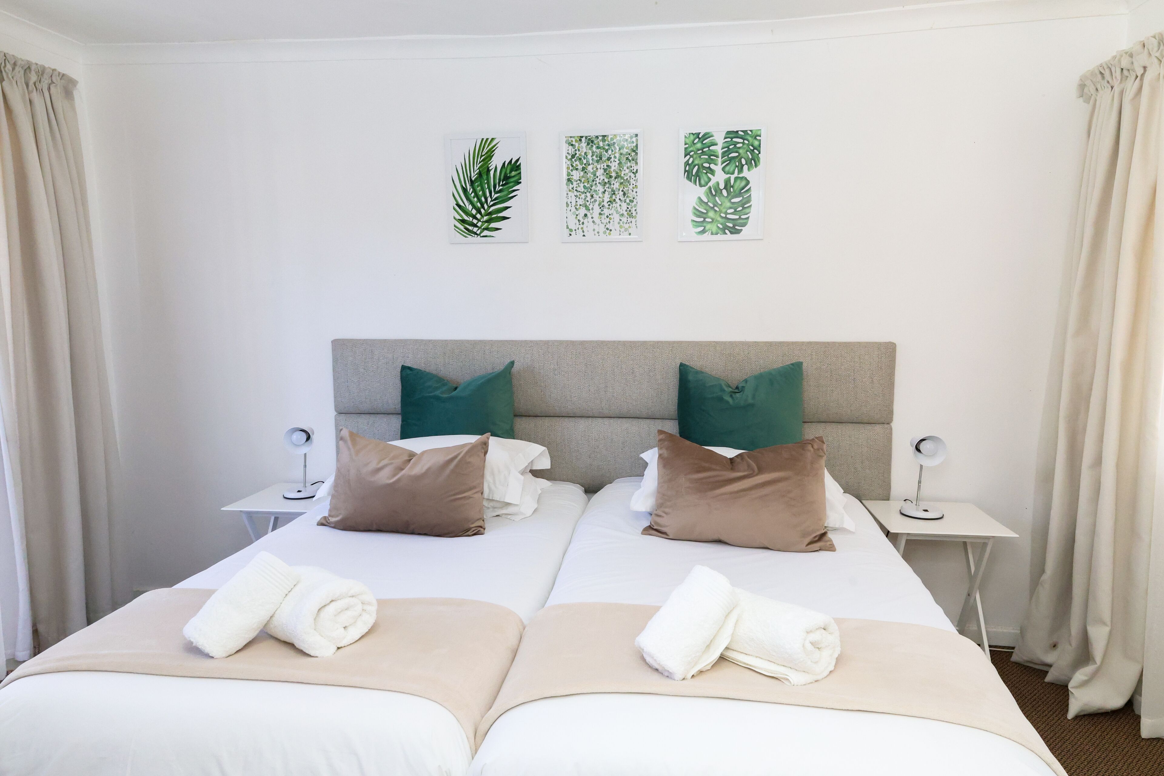 Ein Hotelzimmer mit zwei Betten, beiger Bettwäsche, grünen Kissen und Wandbildern.