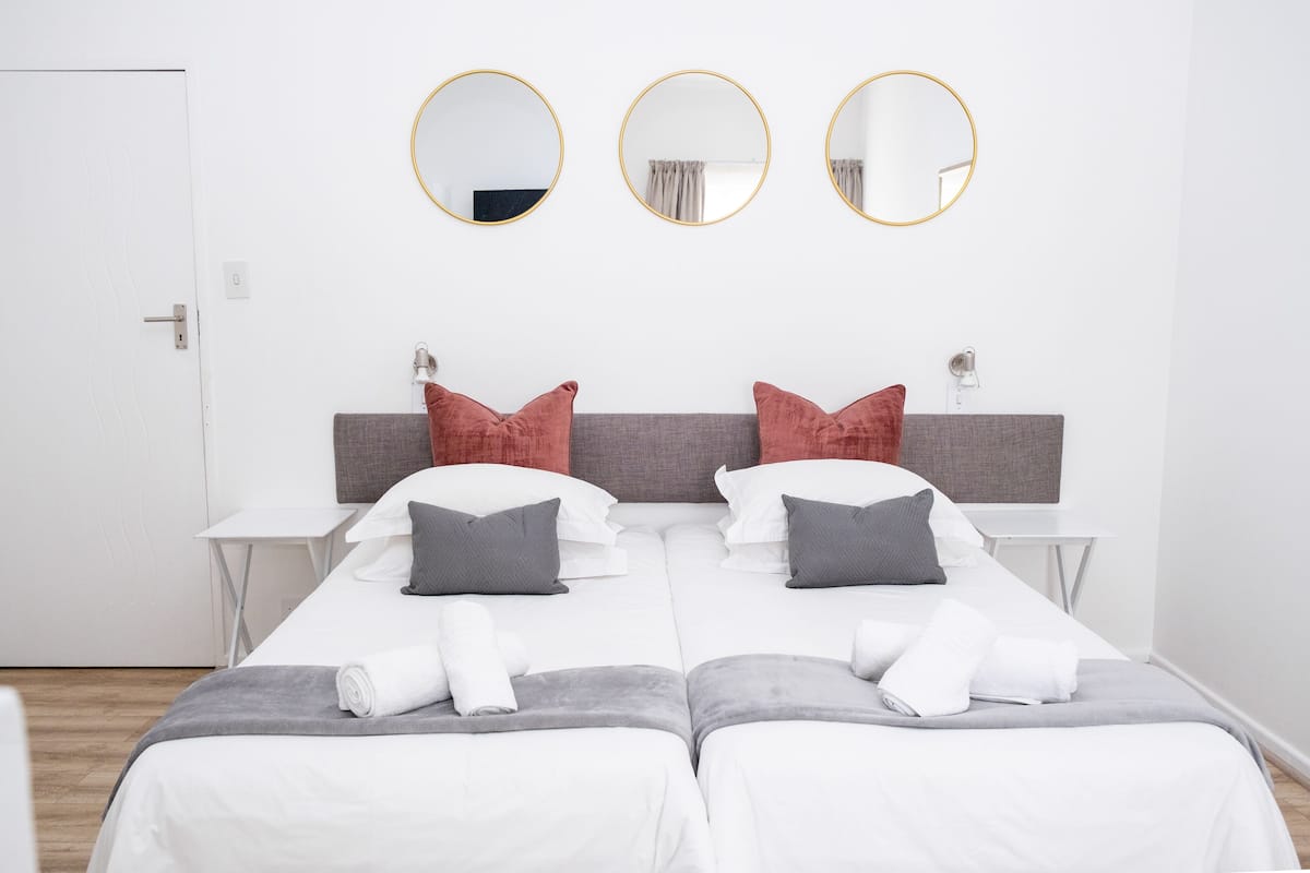 A double room with two beds, a grey headboard, white bedding, and three round mirrors on the wall.