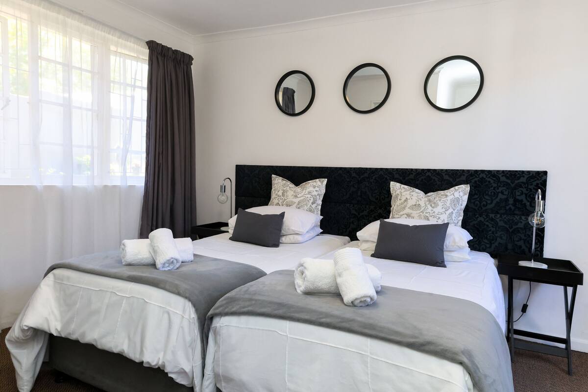 A hotel room with two beds, a dark headboard, and three round mirrors on the wall.