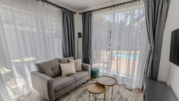 A modern living room with a sofa, two small round tables, and sheer curtains. - George Lodge International (George)